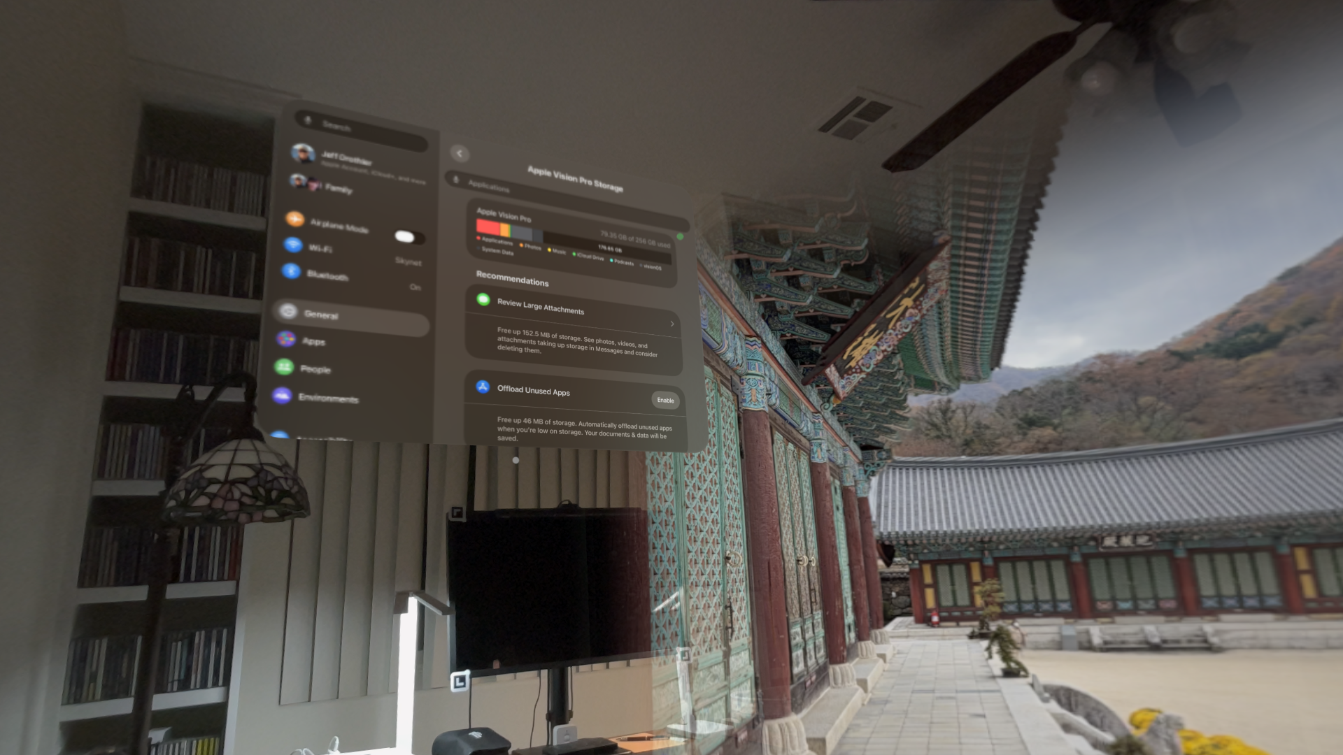 A virtual screen displaying system settings floats in a room with a TV and bookshelf, while the background shows a traditional Asian architectural courtyard and mountainous landscape.